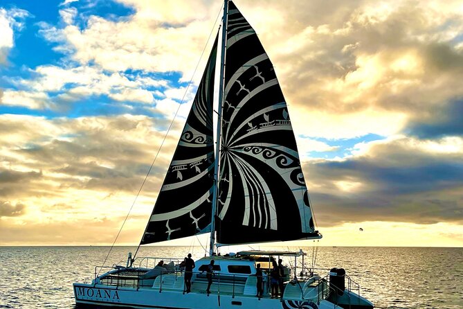A catamaran under full sail off the Waikiki coast at sundown